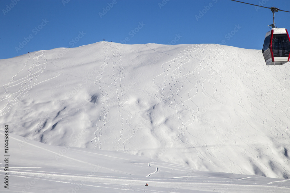 The mountain slope of the ski resort is striated by freeride trails.  A lonely snowboarder at the foot of the mountain.