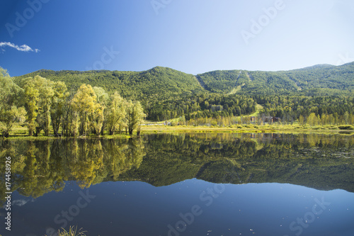Fototapeta Naklejka Na Ścianę i Meble -  Autumn colors of a mountain lake and forests on the banks. Clear reflection of trees on a smooth water surface. A clear, sunny day.