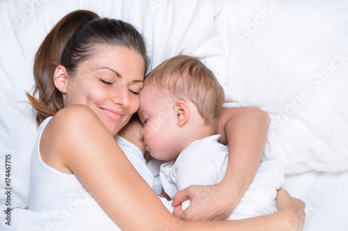 young beautiful mother hugs with her sleeping little cute son on white linen 