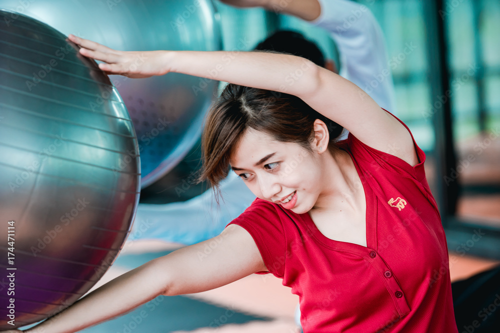 Fototapeta premium Asian teenage girl exercises with a fitness ball in the fitness center with happiness.