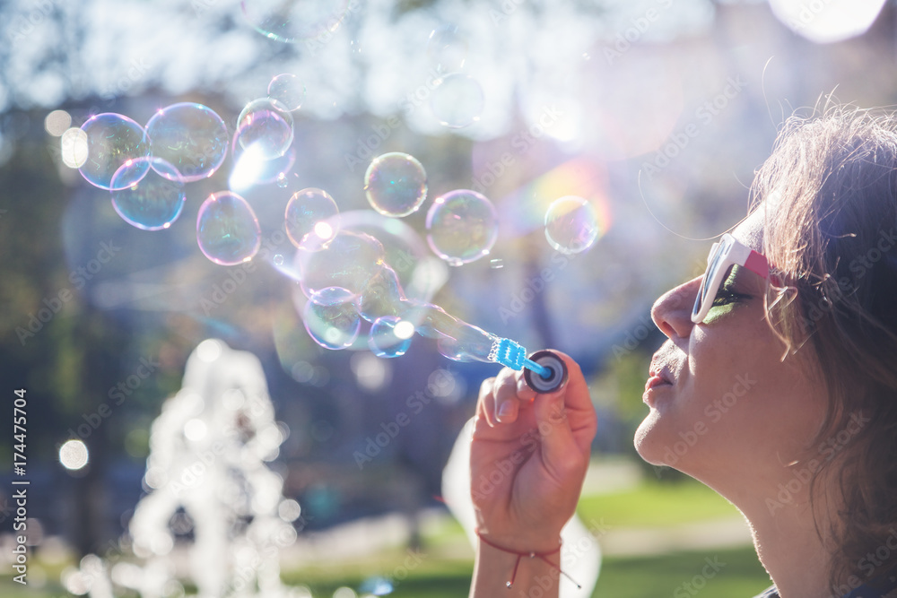 beautiful young woman blowing soap bubbles in the sun
