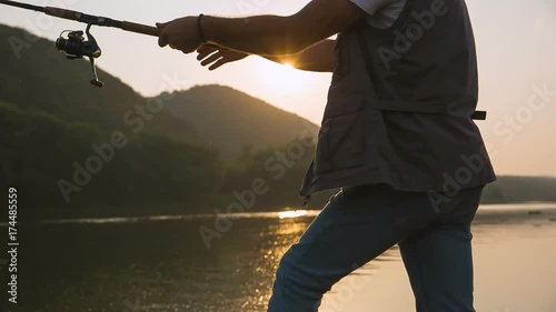 The fisherman rotates the reel on the sunset. Summer evening and sunlight from the water