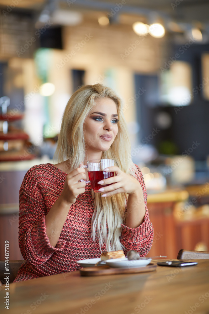 Young fashion woman drinks tea a cafe. caucasian woman sitting in act to drink a cup of tea