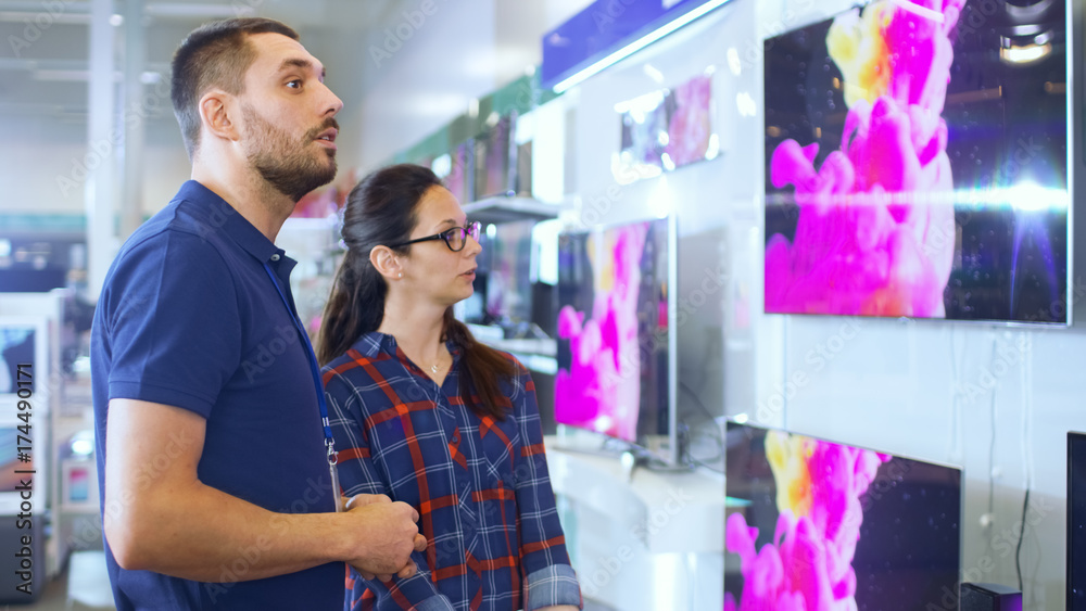 Φωτογραφία In the Electronics Store Professional Consultant Provides Expert Advice to a Young Woman Who Looks for a  New TV to Buy