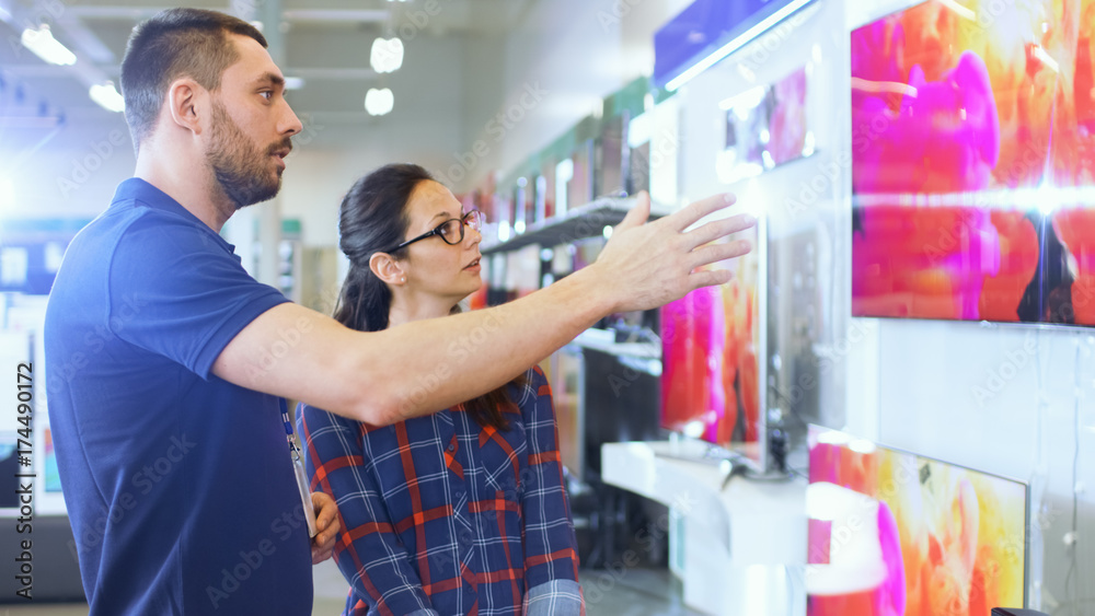In the Electronics Store Professional Consultant Provides Expert Advice to a Young Woman Who Looks for a New TV to Buy. In This Bright, Modern Store. In the Electronics Store Professional Consultant Provides Expert Advice to a Young Woman Who Looks for a New TV to Buy. In This Bright, Modern Store.