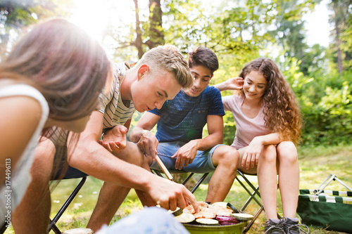 Teenagers camping, cooking vegetables on barbecue grill.