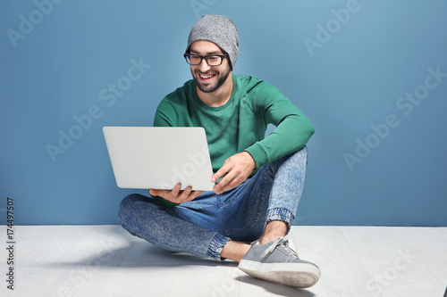 Young blogger with laptop sitting against color wall