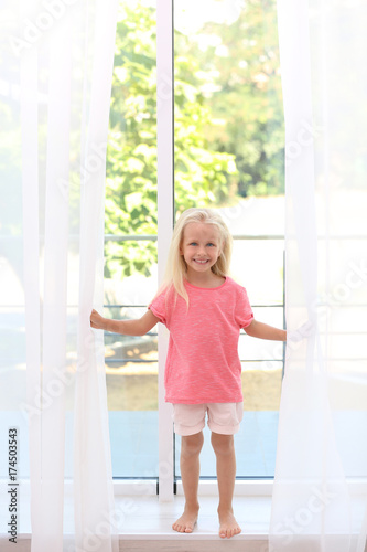 Cute little girl opening curtains at home