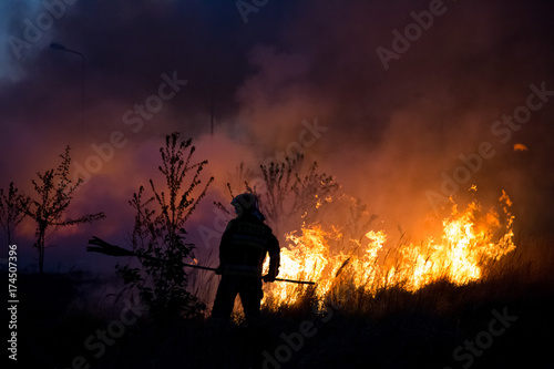Firefighter fighting with bush fire, on the background of flames and burning trees