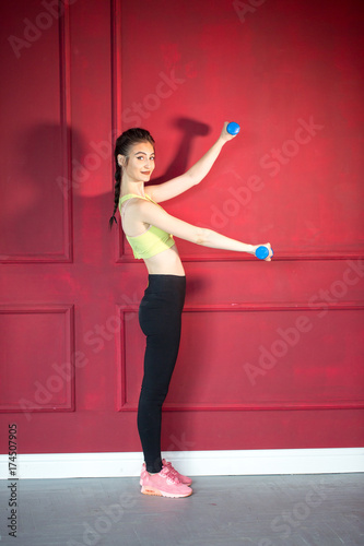 Girl in a yellow swimsuit in the gym teaches yoga with dumbbells