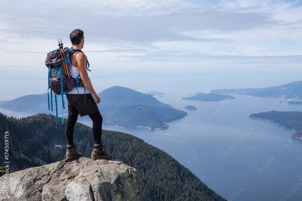 Fit and Adventurous Latin American man is hiking on top of a mountain ridge with a beautiful ocean view in the background. Taken on Lions Peaks, North of Vancouver, British Columbia, Canada.
