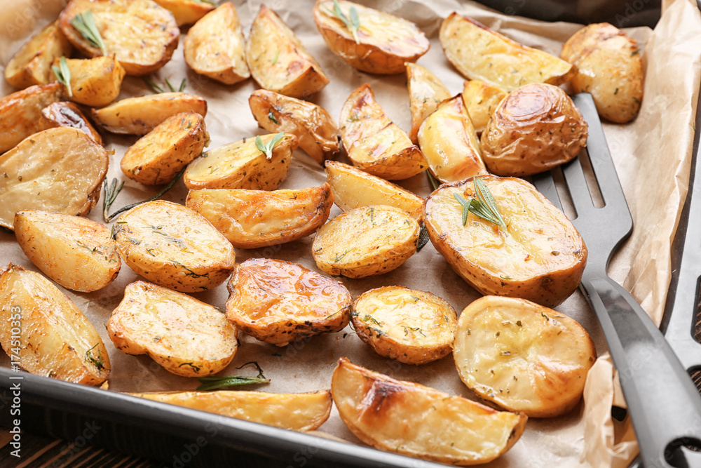 Delicious baked potatoes with rosemary on baking tray, closeup