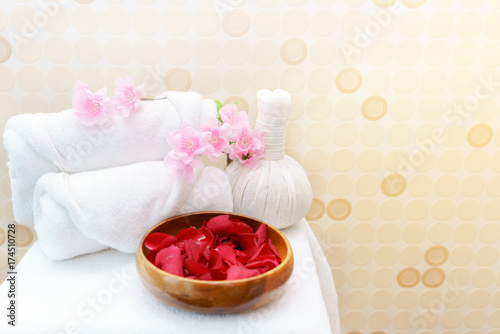 White towel rolls on top with pink flower and Thai Herbal Compress prepared on massage table for spa treatment