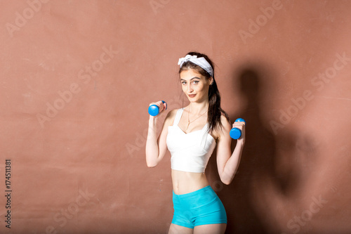Girl in a white swimsuit in the gym teaches yoga with dumbbells