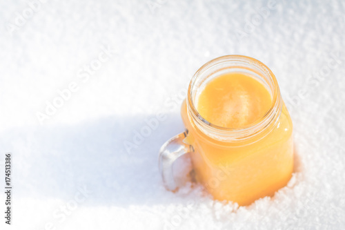 Winter vitamins immunity concept . Freshly squeezed Orange citrus juice for health in glass jar on snow.