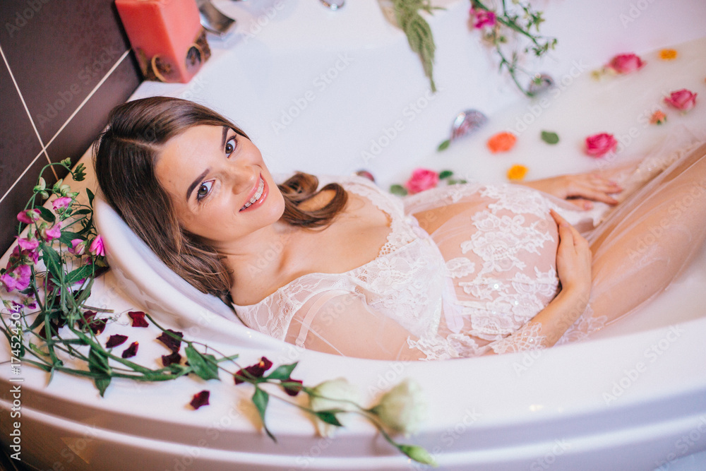 beautiful pregnant woman in a bathroom with milk and flowers.