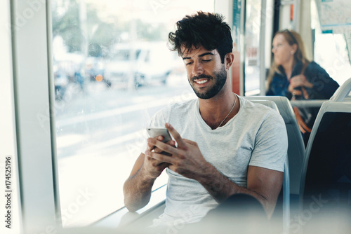 Bearded hipster guy is reading emails on a display of a smartphone connected to public wi-fi while sitting in a city bus. Handsome male is looking at the screen of a mobile phone while texting.