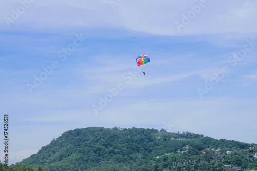 Parachute floats in the sky above the green mountains.