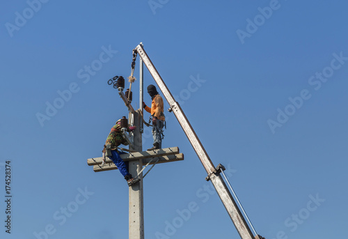 Electricians climbing work on electric power pole with crane on blue sky background