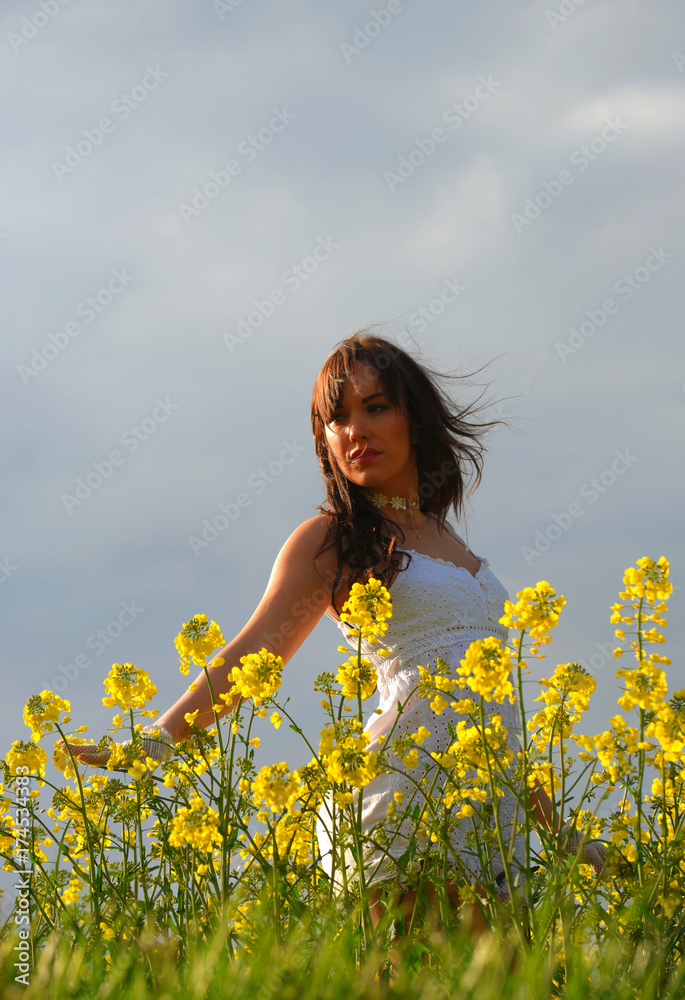 A beautiful young girl strolls through a rape seed field on a summer evening. Feeling carefree and serene she admires the colorful yellow flowers as the sun passes through them. A beautiful young girl strolls through a rape seed field on a summer evening. Feeling carefree and serene she admires the colorful yellow flowers as the sun passes through them.