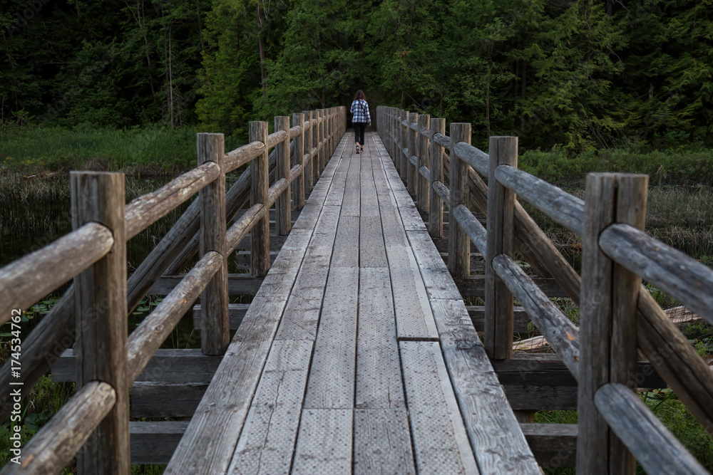 Wooden bridge across swampy water with woman walking across it. Taken in Brohm Lake, between Squamish and Whistler, North of Vancouver, BC, Canada.