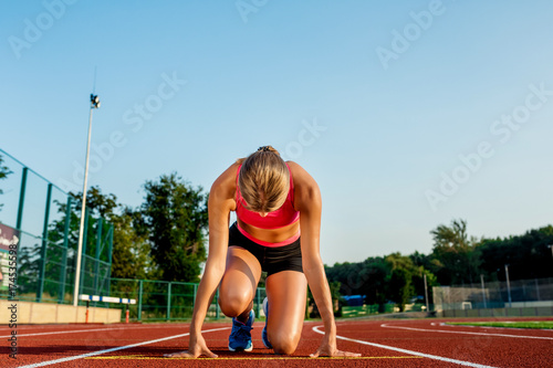 Young woman athlete at starting position ready to start a race on racetrack.