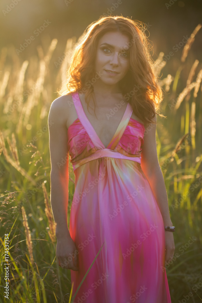 Portrait of a attractive woman posing in summer meadow at sunset