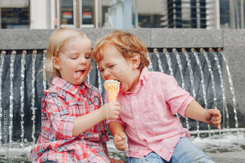 Fényképezés Group portrait of two white Caucasian cute adorable funny children toddlers sitting together sharing ice-cream food