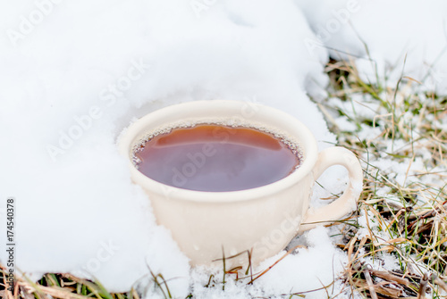 Nice warm cup of tea or coffee outdoors on the snow on a background of a winter landscape. Cozy winter still life.
