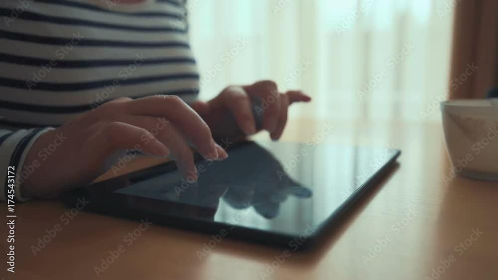 Woman typing e-mail reply on digital tablet computer. Close up of adult caucasian female hands using personal electronics device and wireless internet to communicate from her living room in morning. Woman typing e-mail reply on digital tablet computer. Close up of adult caucasian female hands using personal electronics device and wireless internet to communicate from her living room in morning.