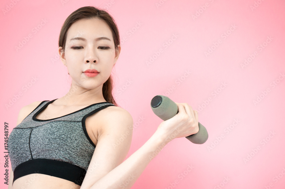 Asian beauty woman in sport bar exercise by lifting dumbbell on pink background