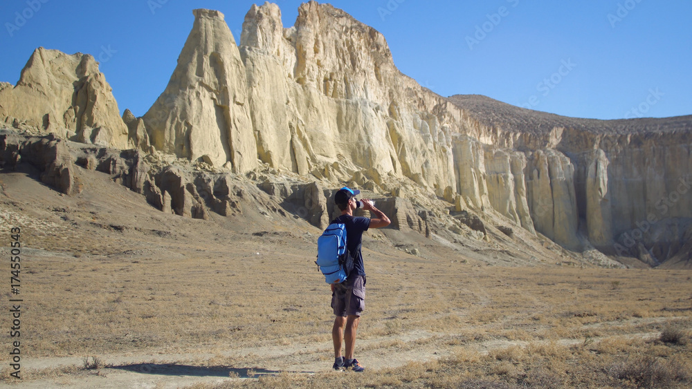 A young traveler drinks water against the rocks