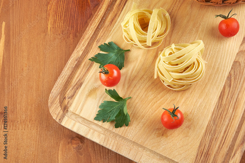Tomatoes in a wicker basket and green leaves of salad, pasta nests on a wooden Board Tomatoes in a wicker basket and green leaves of salad, pasta nests on a wooden Board