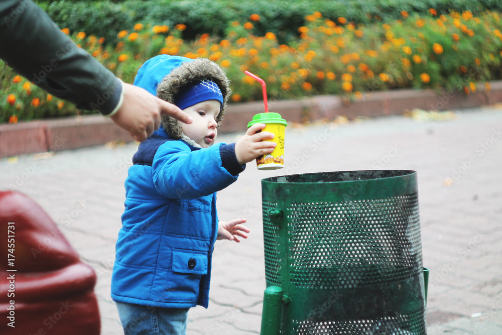 A small child in the street throws a paper glass in the trash can. His