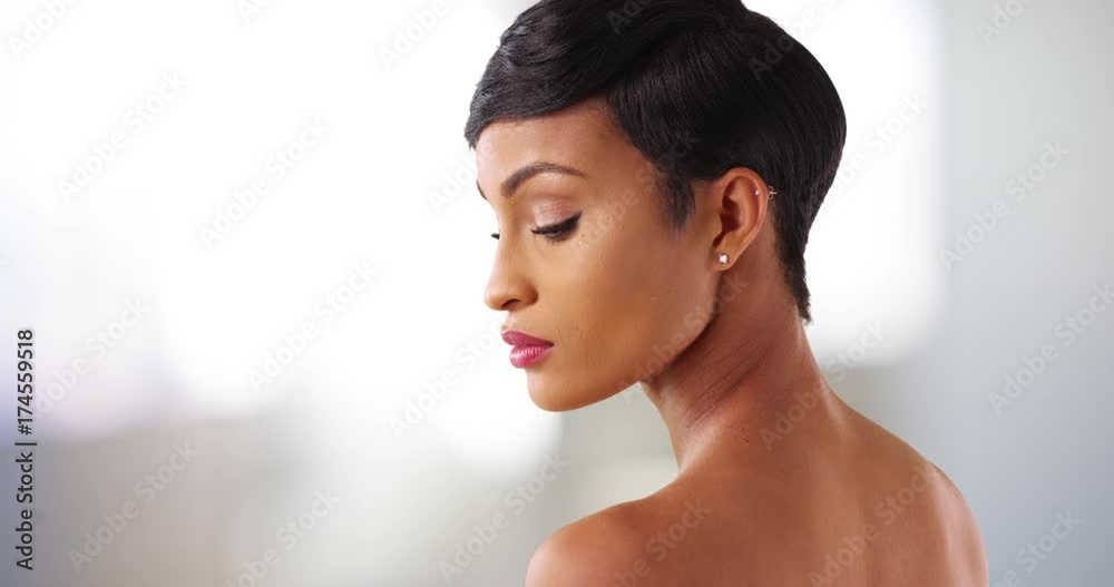 Close up of gorgeous black female with bare shoulders looking down. Portrait of lovely African American woman in her 20s modeling 