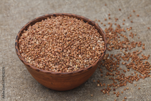 Healthy buckwheat groats in bowl on the burlap background closeup