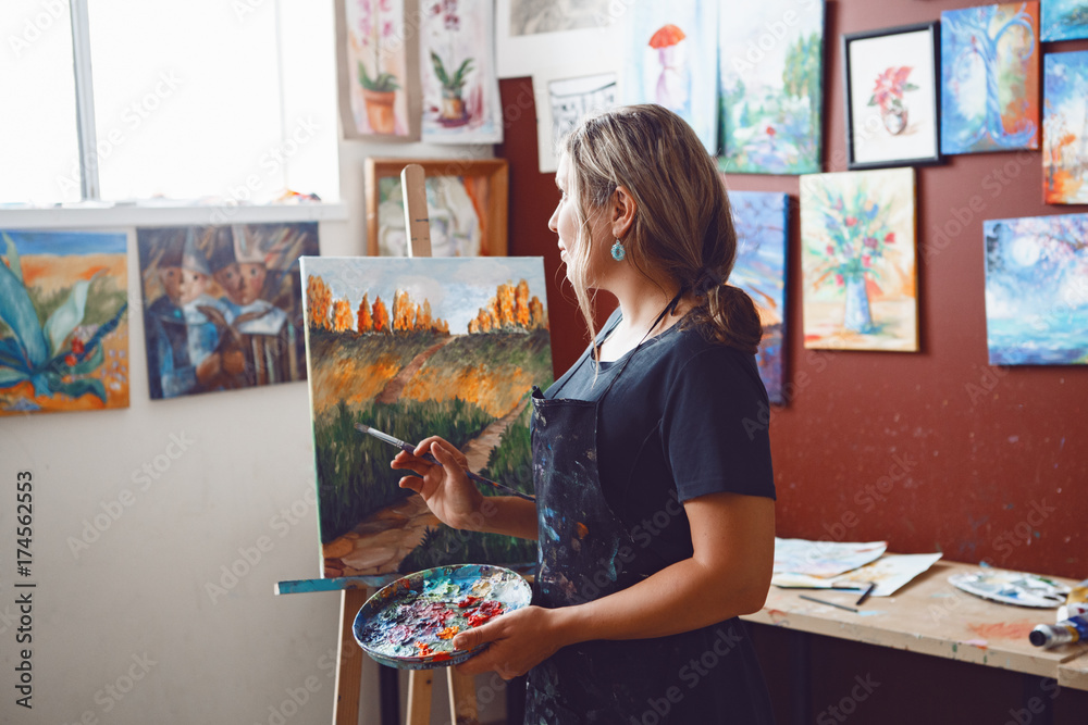 Fototapeta premium Portrait of young beautiful middle age white Caucasian woman artist drawing painting in art studio with acrylic paints on canvas. Lifestyle activity hobby concept