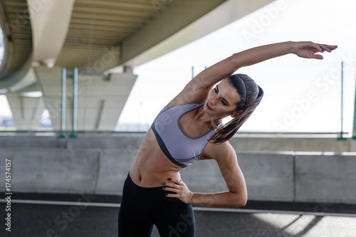 Caucasian fitness model stretching body. Young woman doing exercises under a bridge. © Artem Varnitsin