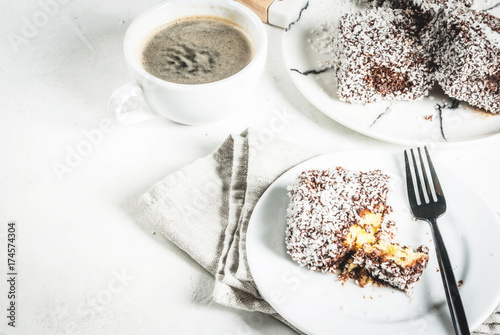Australian food. Traditional dessert Lamington - pieces of biscuit in dark chocolate  sprinkled with coconut powder chips. On a marble plate  white table. With coffee mug. Copy space