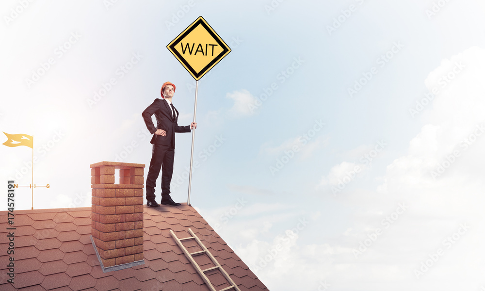 Young businessman on house brick roof holding yellow signboard. Young businessman on house brick roof holding yellow signboard.