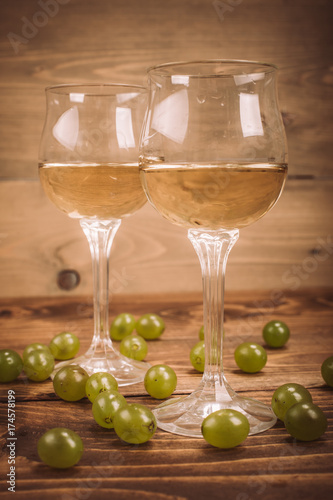 Two glasses of white wine and grapes on wooden table