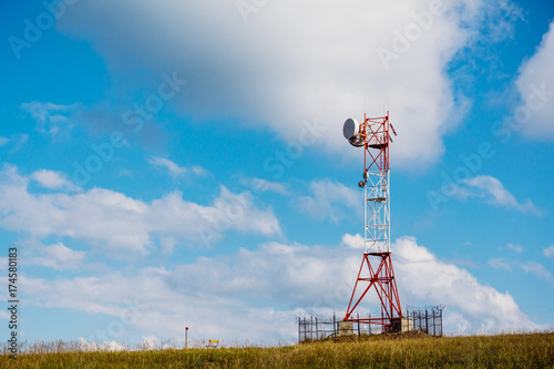Communication tower for mobile communications and TV antennas on mountain hill at blue sky background
