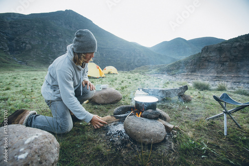 outdoorsman stoking a cooking fire whilst camping in the mountains