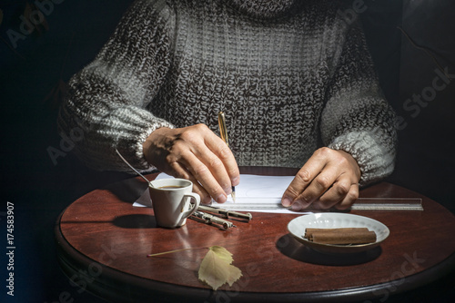 Male hands, at the table and write a pen on a piece of paper on a dark background
