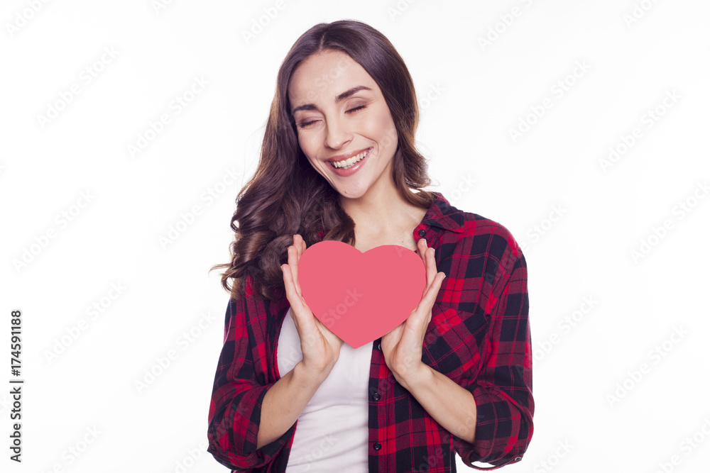 Young beautiful brunette girl smiles and holds in her hands a red paper heart isolated on white Young beautiful brunette girl smiles and holds in her hands a red paper heart isolated on white