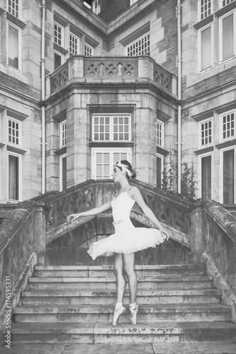 Pretty ballerina dancing on white tutu, at palace entrance stairs, vintage photo on black and white with grain efect