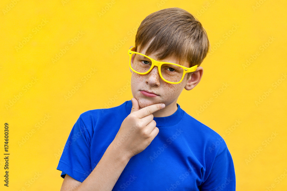 Serious freckled boy looking at camera, touching chin and thinking. Serious freckled boy looking at camera, touching chin and thinking.