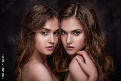 Fashion studio picture of two twins beautiful women. Close-up beauty portrait of sisters models.