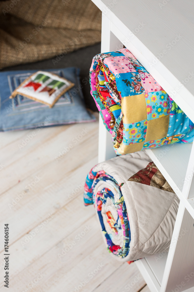 patchwork, sewing and fashion concept - two colorful quilted bedspreads in studio at white shelves with few storage compartments, warehouse of finished products, pillow on floor, top view, vertical