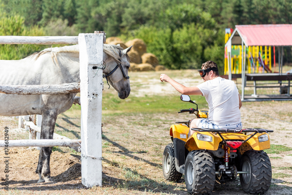 Obraz premium Caucasian man on ATV quad bike meet beautiful white horse on a farm or ranch. Evolution of vehicles for centuries concept. Past and present progress